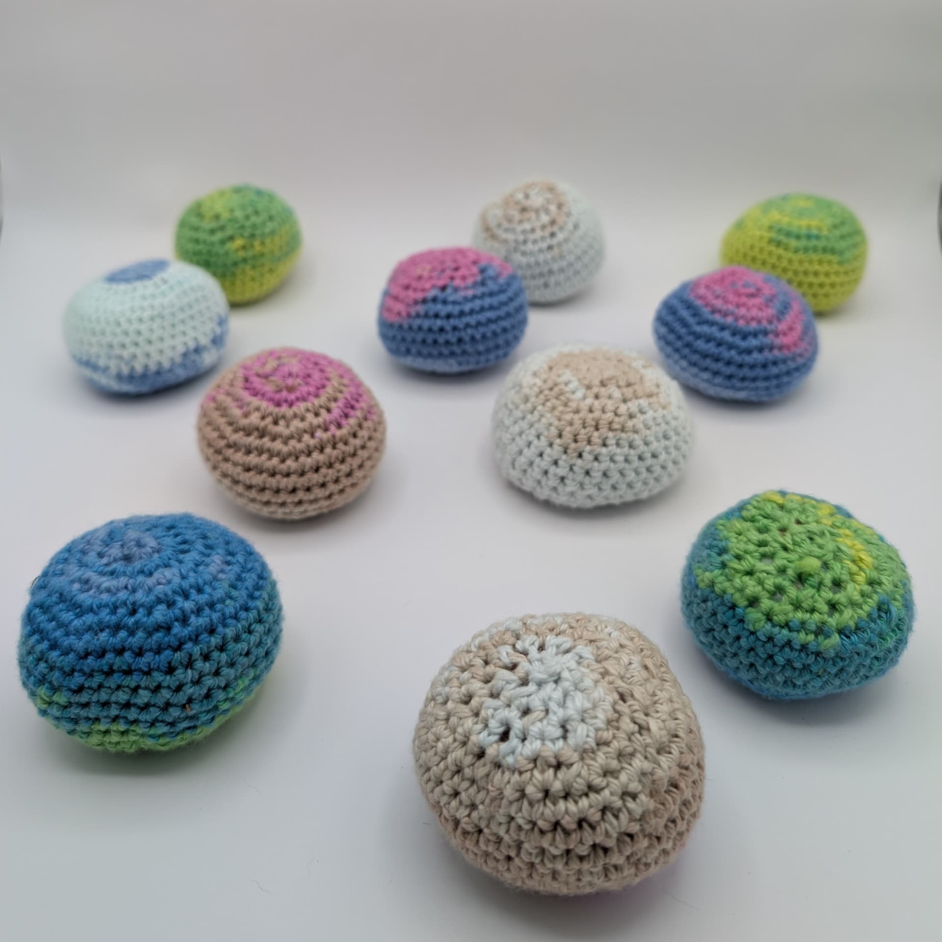 Collection of handmade crochet hacky sacks in assorted colors, including blue, pink, green, and neutral cotton yarn.